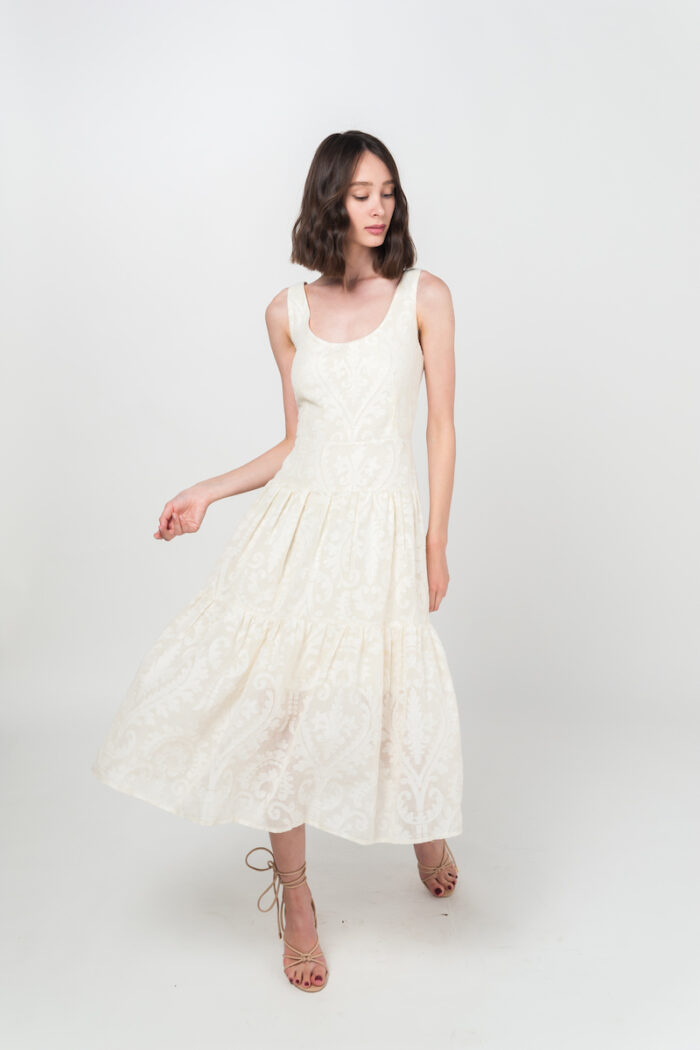 Devojka kratke braon kose nosi elegantnu letnju JOVANA haljinu od pamuka sa floralnom teksturom u bež-beloj boji.