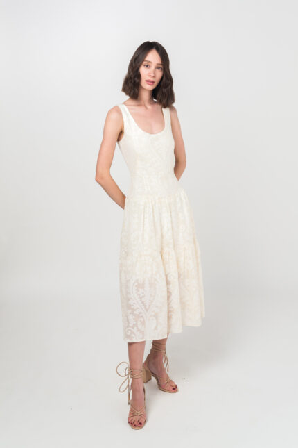 Devojka kratke braon kose nosi elegantnu letnju JOVANA haljinu od pamuka sa floralnom teksturom u bež-beloj boji.