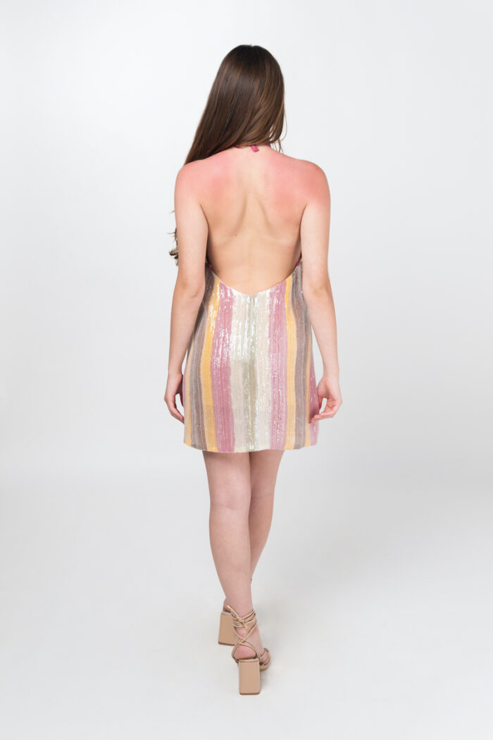 Devojka nosi kratku haljinu HELENICA od šarenog svetlucavog materijala.