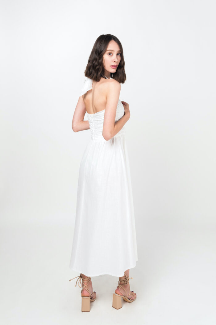 Devojka nosi dugu belu haljinu za leto, na bretele, sa otvorenim leđima.