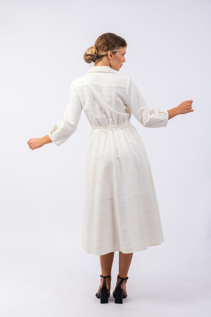 Plava devojka nosi midi belu JELENA haljinu od šantung svile sa belim biserima.