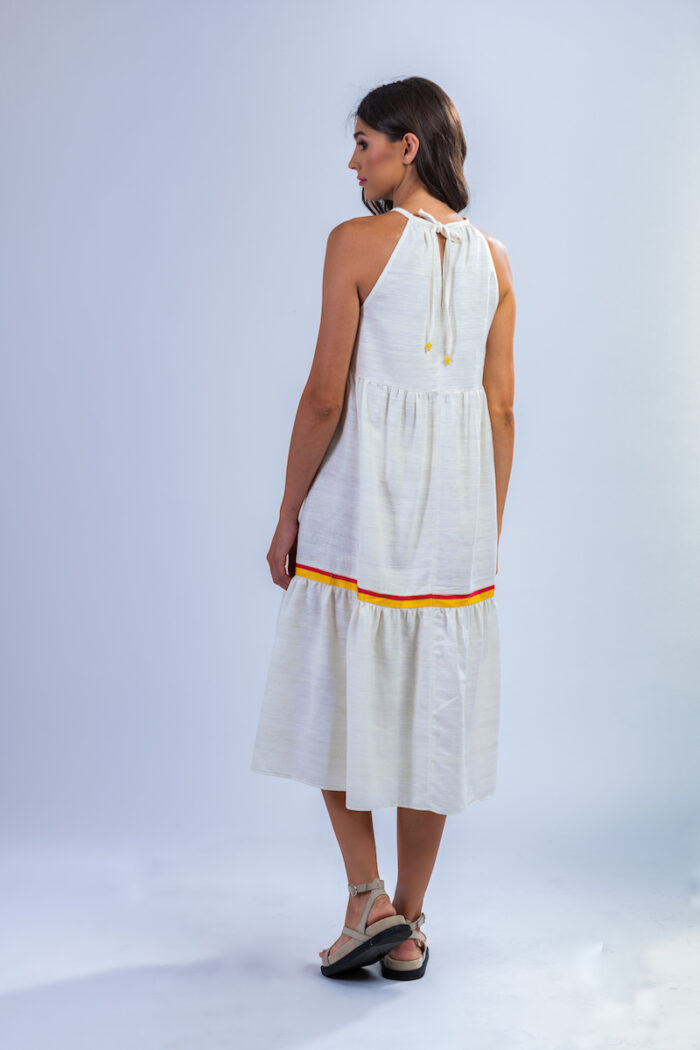 Devojka nosi midi belu haljinu za leto od šantung svile sa raznobojnim lanenim detaljima.