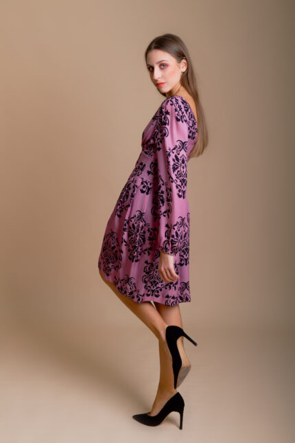 Girl wears short MARIA dress crafted from patterned silk in luxurious shade of purple with black floral details.
