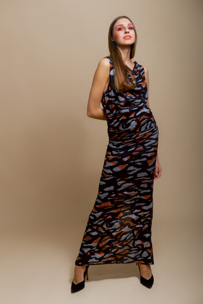 Devojka nosi dugu svilenu MIRNA haljinu tigrastog printa ispred bež pozadine.