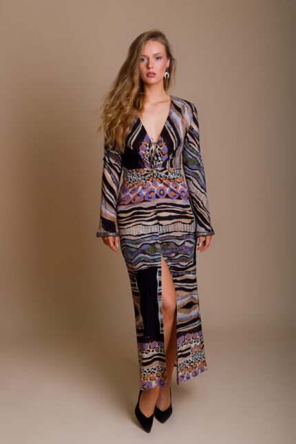 The girl wears the UNA dress made of patterned silk in an animal print, with lots of designer details. The girl wears black shoes with high heels and stands in front of a beige background.