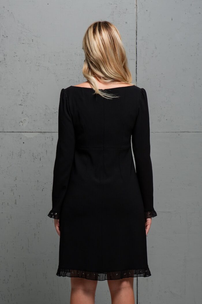 Plava devojka nosi crnu haljinu midi dužine i stoji ispred sive pozadine.