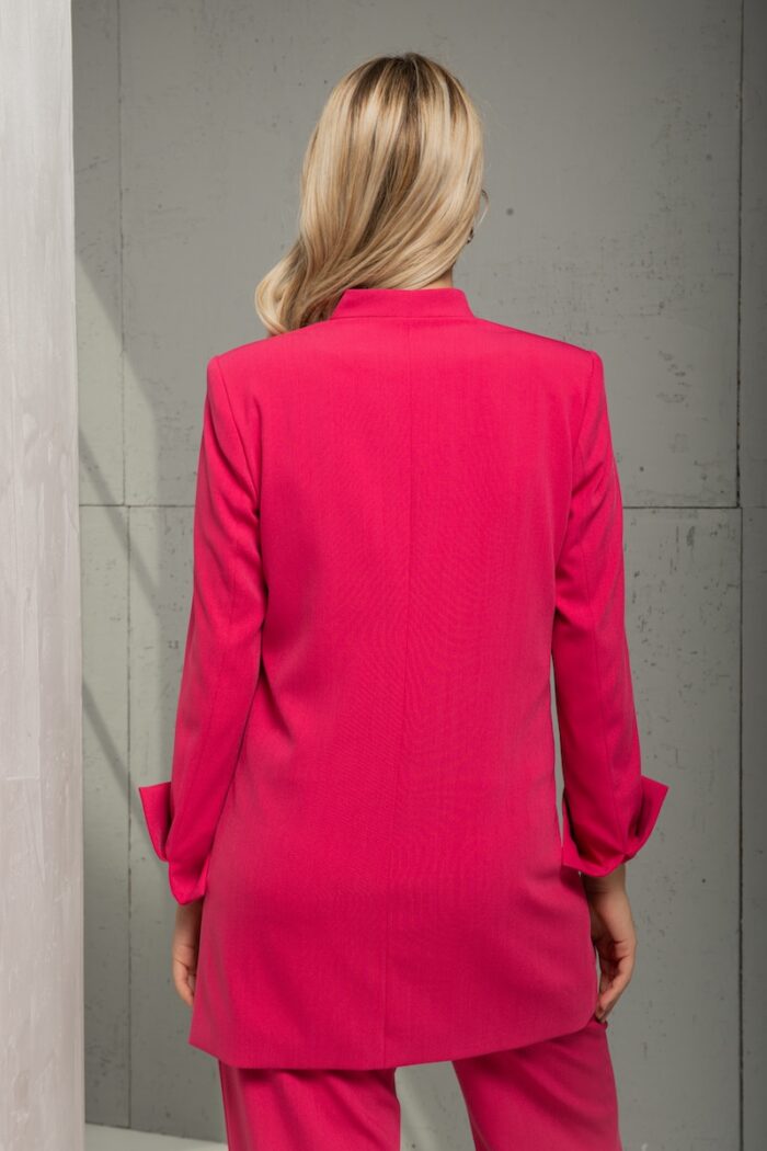 Blonde girl is wearing a cyclamen LIVIA blazer with a slightly oversized cut and is standing in front of a gray background.