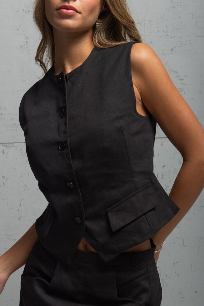 Brunette is wearing a black vest made of cotton twill and standing in front of a gray background.