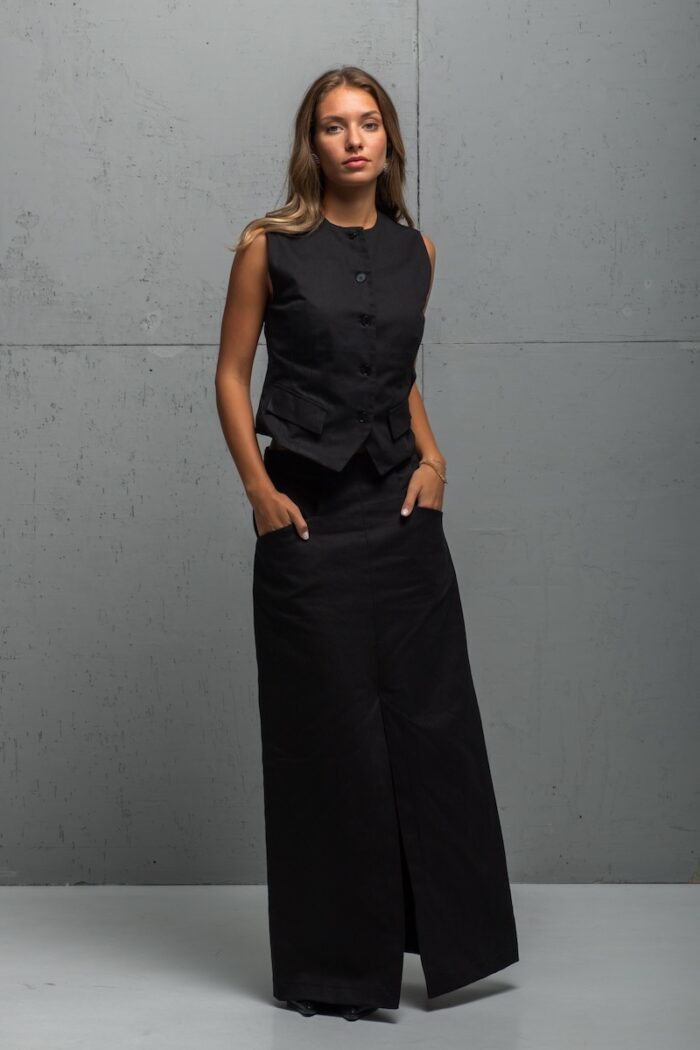 Brineta nosi crni LOU prsluk i suknju od pamučnog kepera i stoji ispred sive pozadine.