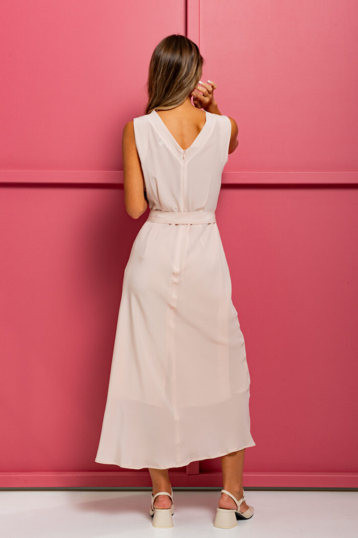 The girl is wearing a midi silk dress in powder pink color without sleeves, standing in front of a pink background.