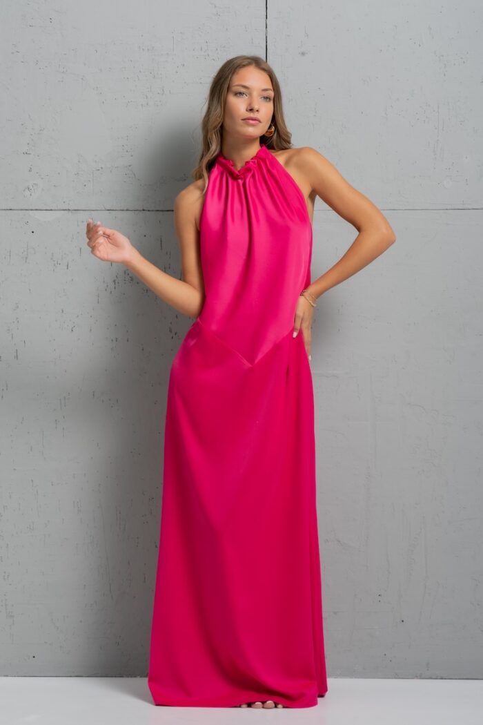 Brineta nosi dugu pink haljinu od satena i stoji ispred sivog zida.