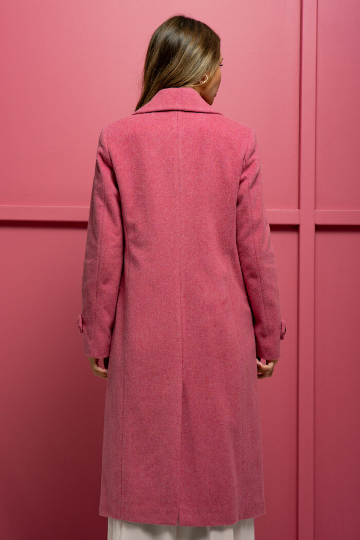 The girl is wearing a pink wool coat with double-breasted closure and standing in front of a pink background