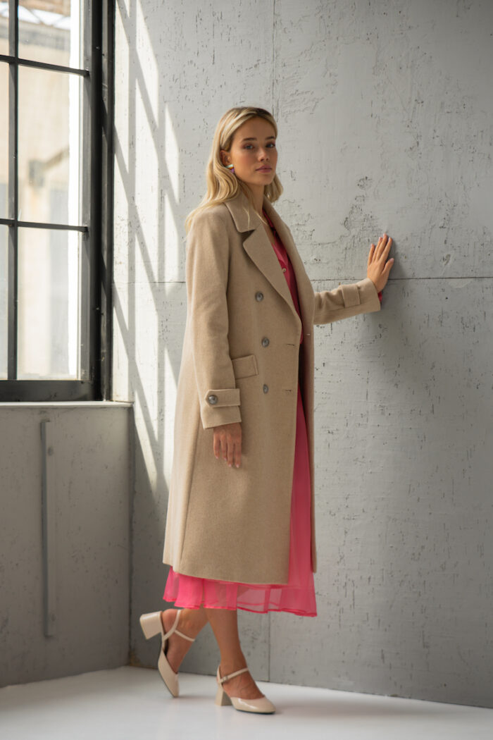 The blonde girl is wearing a long beige coat with a pink combination underneath