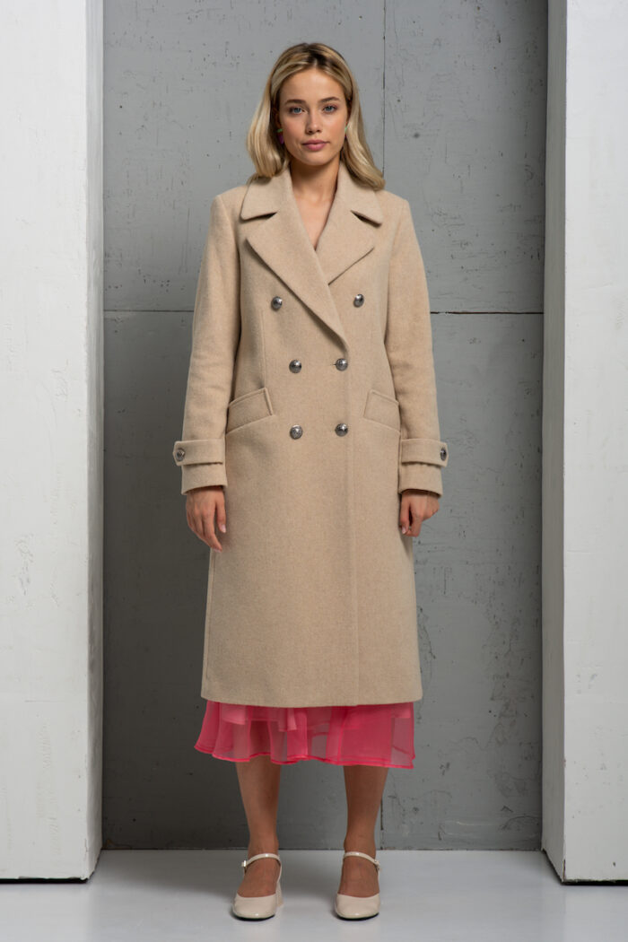 The blonde girl is wearing a long beige coat with a pink combination underneath