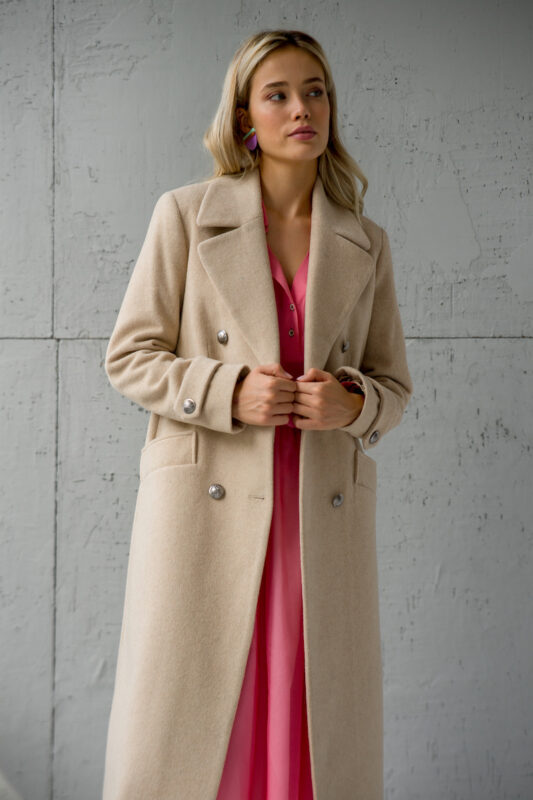 The blonde girl is wearing a long beige coat with a pink combination underneath.