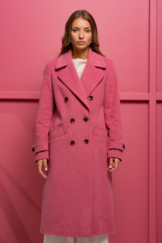 The girl is wearing a pink wool coat with double-breasted closure and standing in front of a pink background.