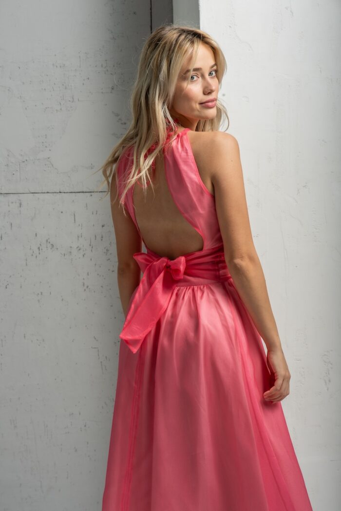 The blonde girl is wearing a pink ASTRA top made of silk organdy with a skirt made from the same material. She is standing in front of a gray wall.