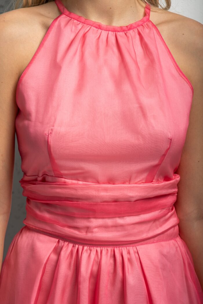 Plava devojka nosi roze ASTRA top od svilenog organdina sa suknjom od istog materijala. Stoji ispred sivog zida.