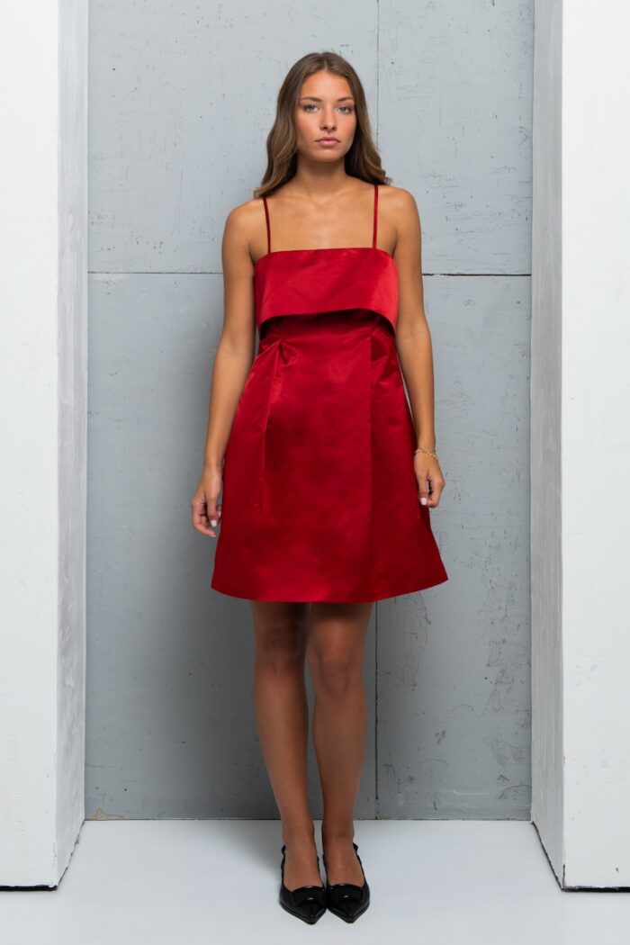 Devojka nosi kratku MADLENA haljina od satenskog materijala u tamno-crvenoj boji.