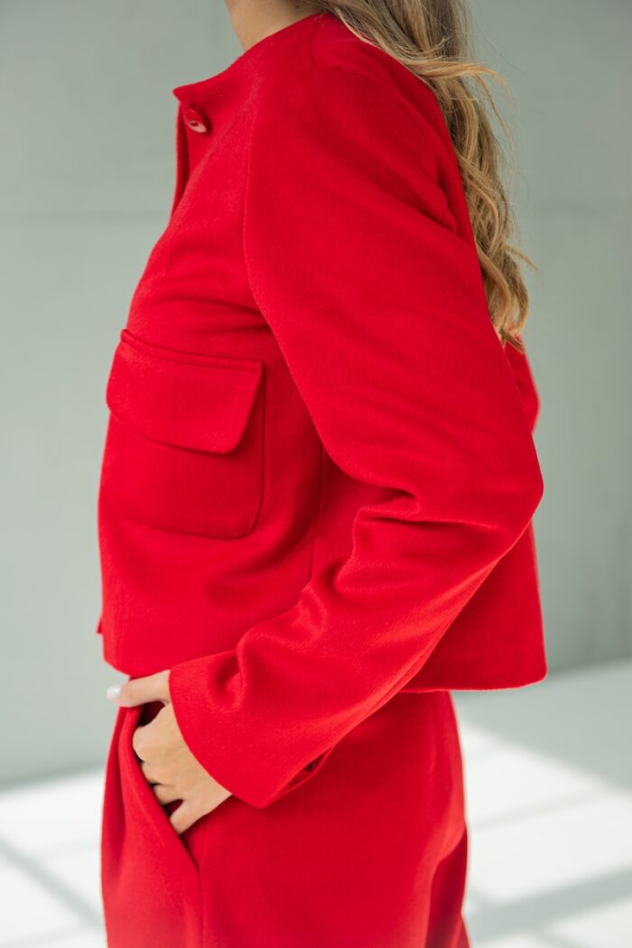 Devojka nosi crveni RUBY sako i stoji ispred sivog zida.