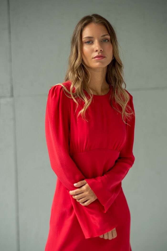 Devojka nosi kratku crvenu TEONA haljinu od svile sa dugim rukavima.