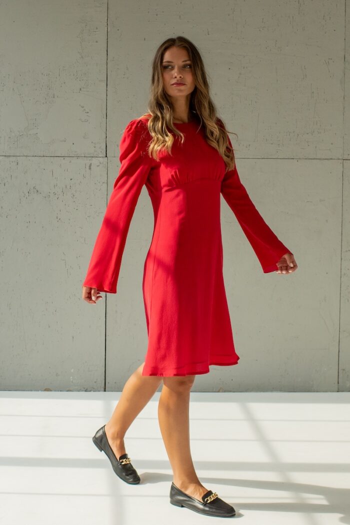 Devojka nosi kratku crvenu TEONA haljinu od svile sa dugim rukavima.