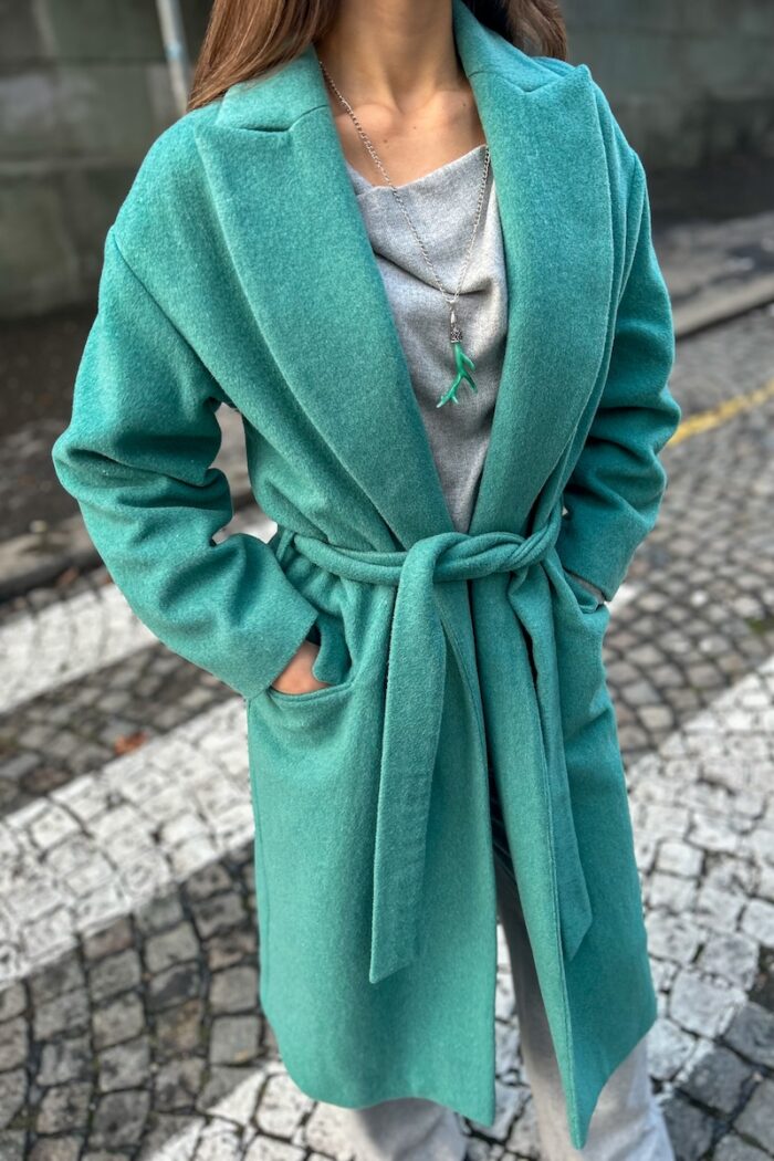 Devojka nosi zeleni CHARLOTTE kaput na vezivanje i drži ruke u džepovima.