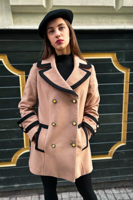The girl is wearing a beige TEODORA coat with double-breasted closure and has her hands in the pockets.