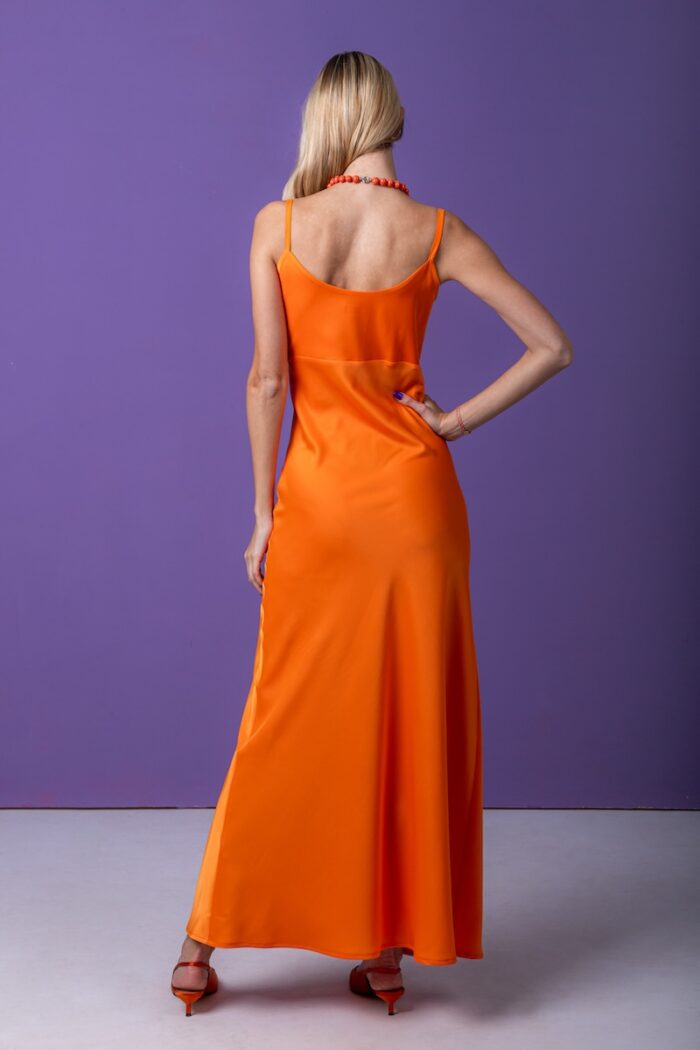 Blonde girl, long orange dress, purple background, suspenders, orange necklace.