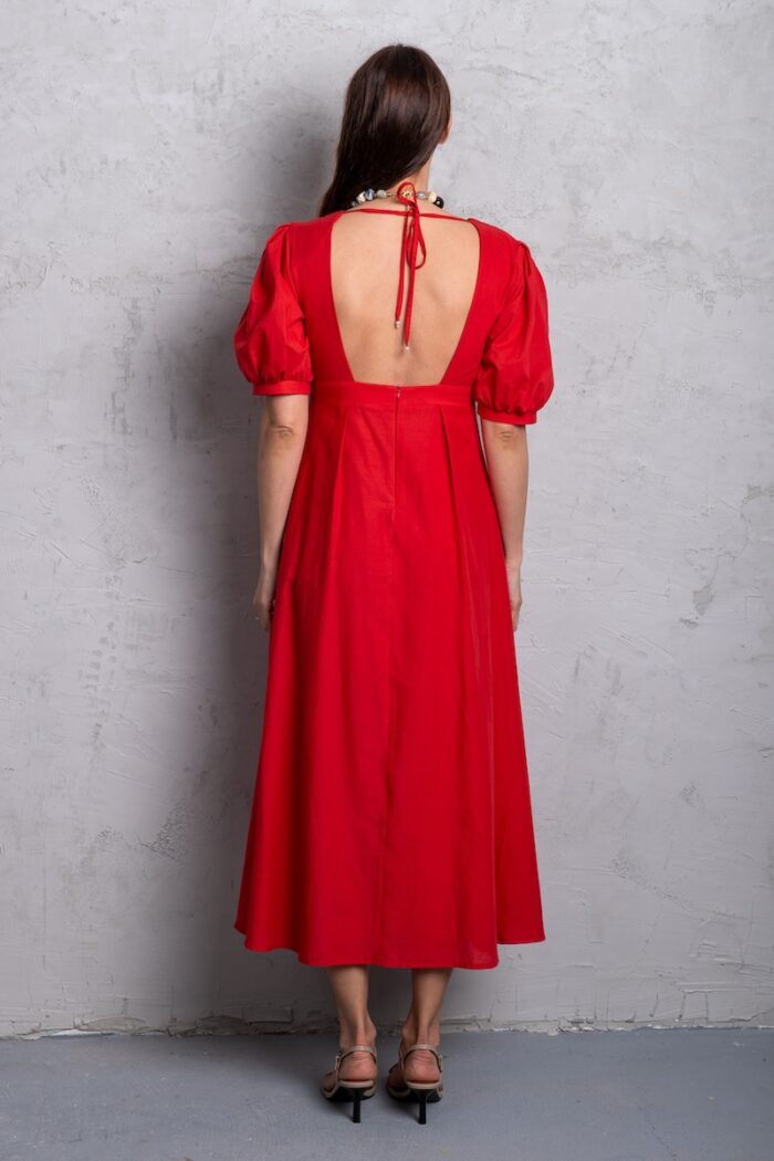 Model nosi crvenu haljinu midi dužine sa puf rukavima i V izrezom.