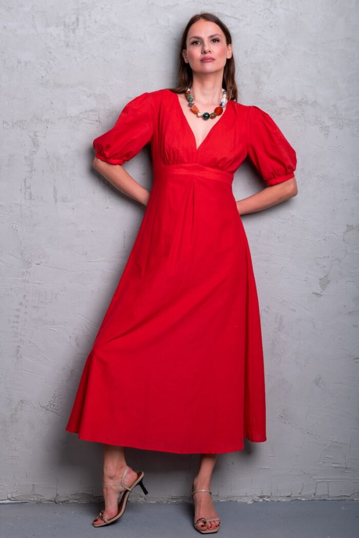 Model nosi crvenu haljinu midi dužine sa puf rukavima i V izrezom.