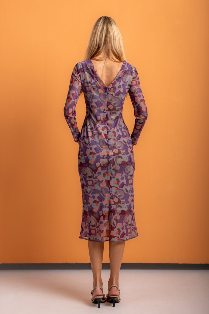 A blonde girl wears a patterned midi-length dress and stands in front of an orange background.