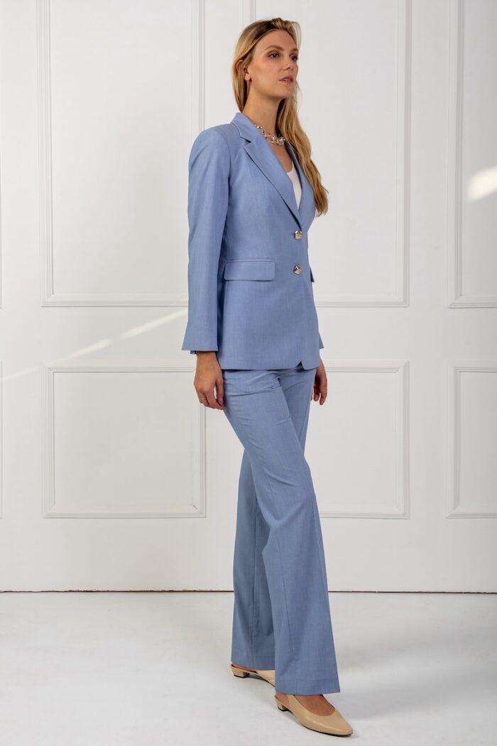 A blonde girl wears a blue blazer and stands in front of a white wall.