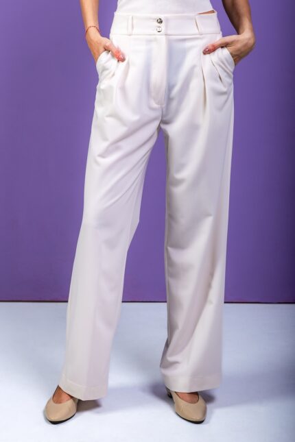 The blonde girl is wearing wide-leg trousers and standing in front of a purple background.