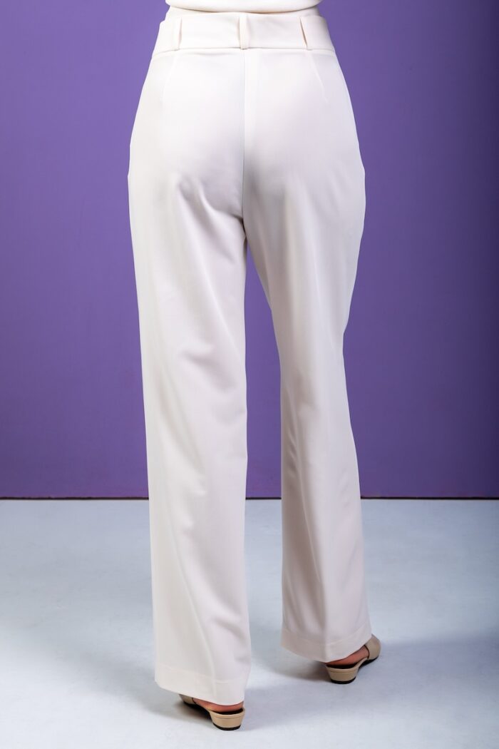 The blonde girl is wearing wide-leg trousers and standing in front of a purple background.