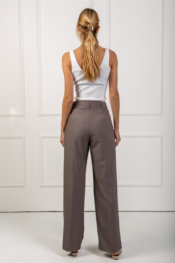 The blue girl wears wide brown trousers and a white top, standing in front of a white wall.