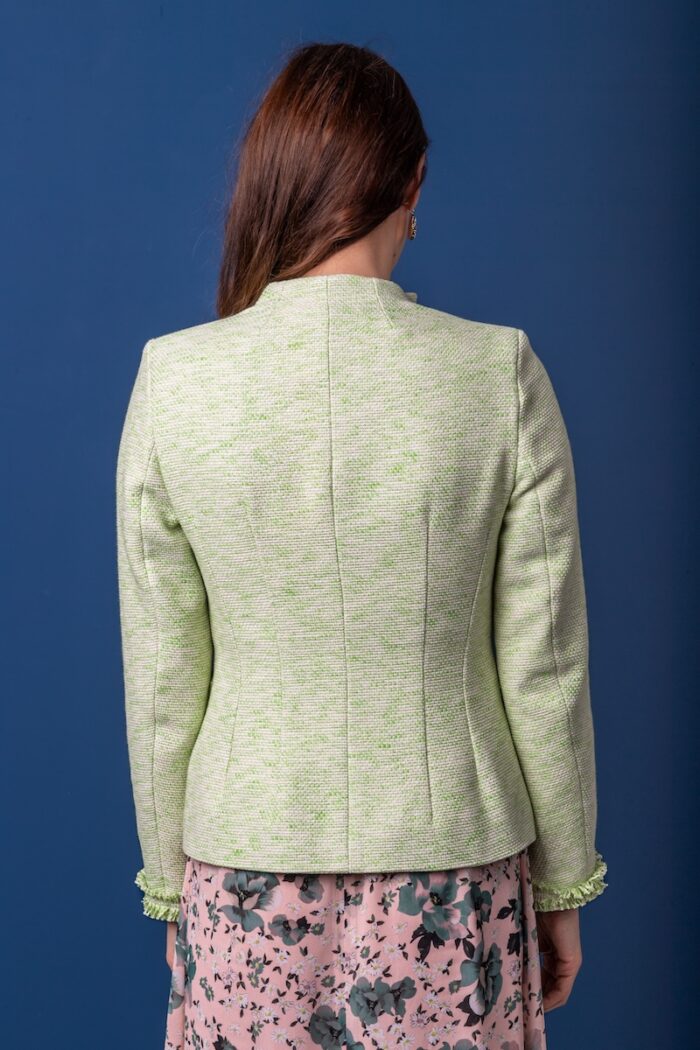 A woman wears a green cotton blazer and floral dress and stands in front of a blue background.